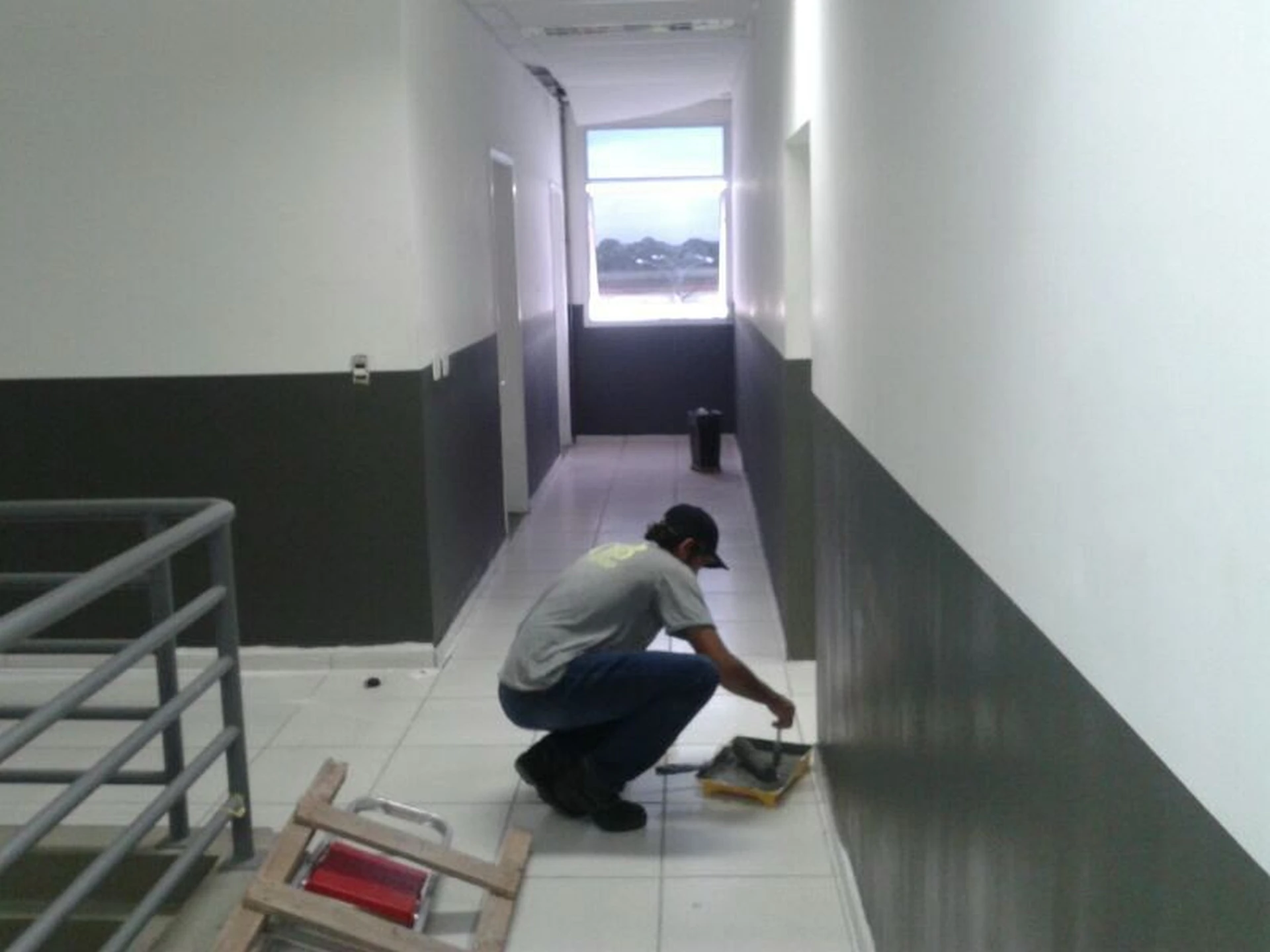 Trabalhador aplicando pintura de acabamento na parte inferior da parede de corredor