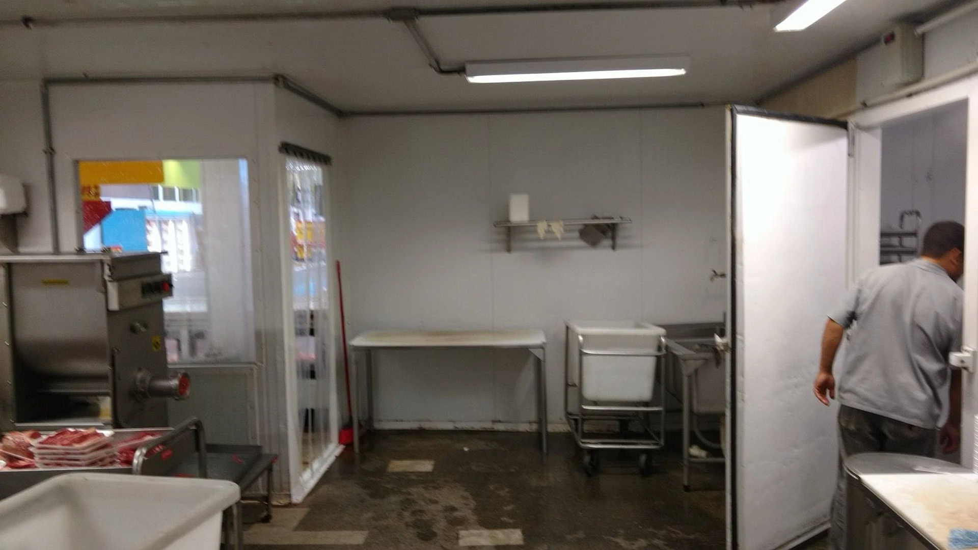 Setor de processamento de carnes em operação com equipamentos industriais e câmara frigorífica ao fundo