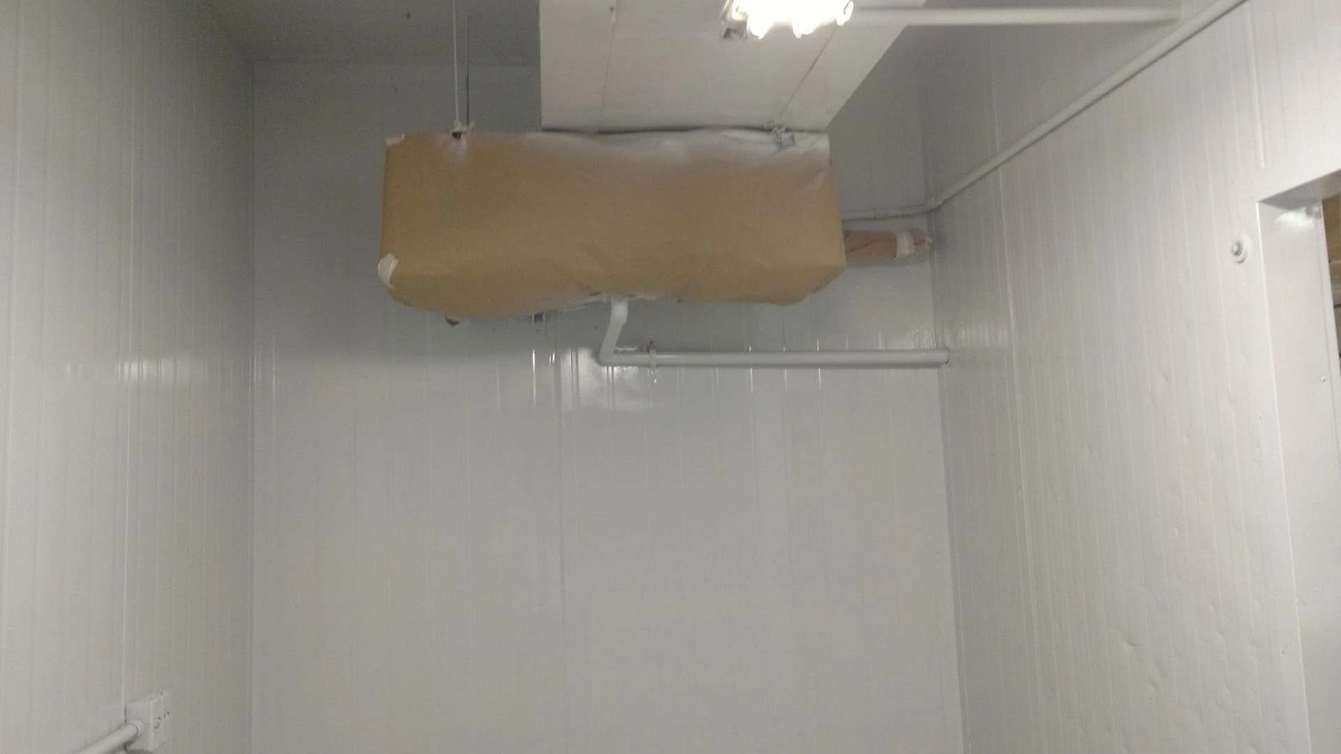 Interior da câmara com novos painéis instalados e evaporador protegido com papel durante serviços