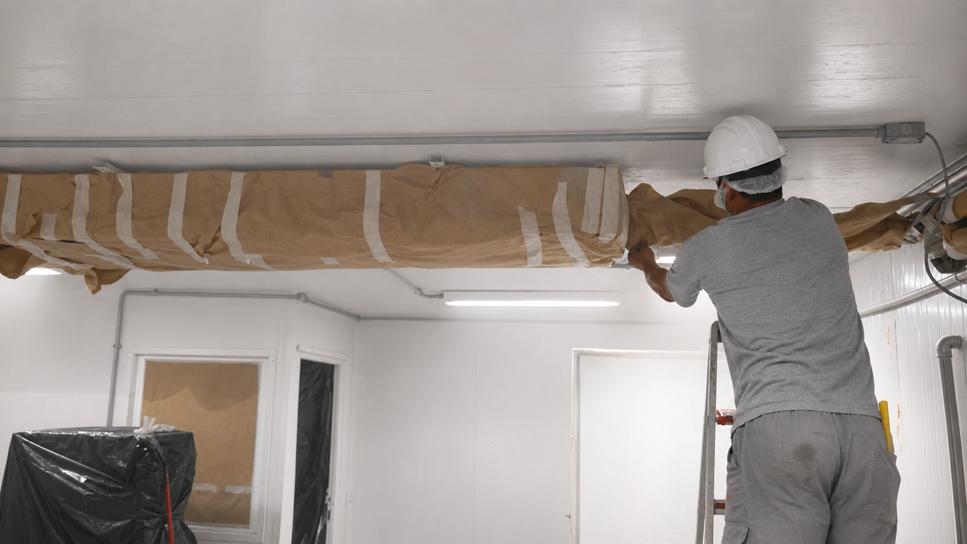 Trabalhador removendo proteção do trilho de câmara após conclusão da pintura e instalação dos painéis